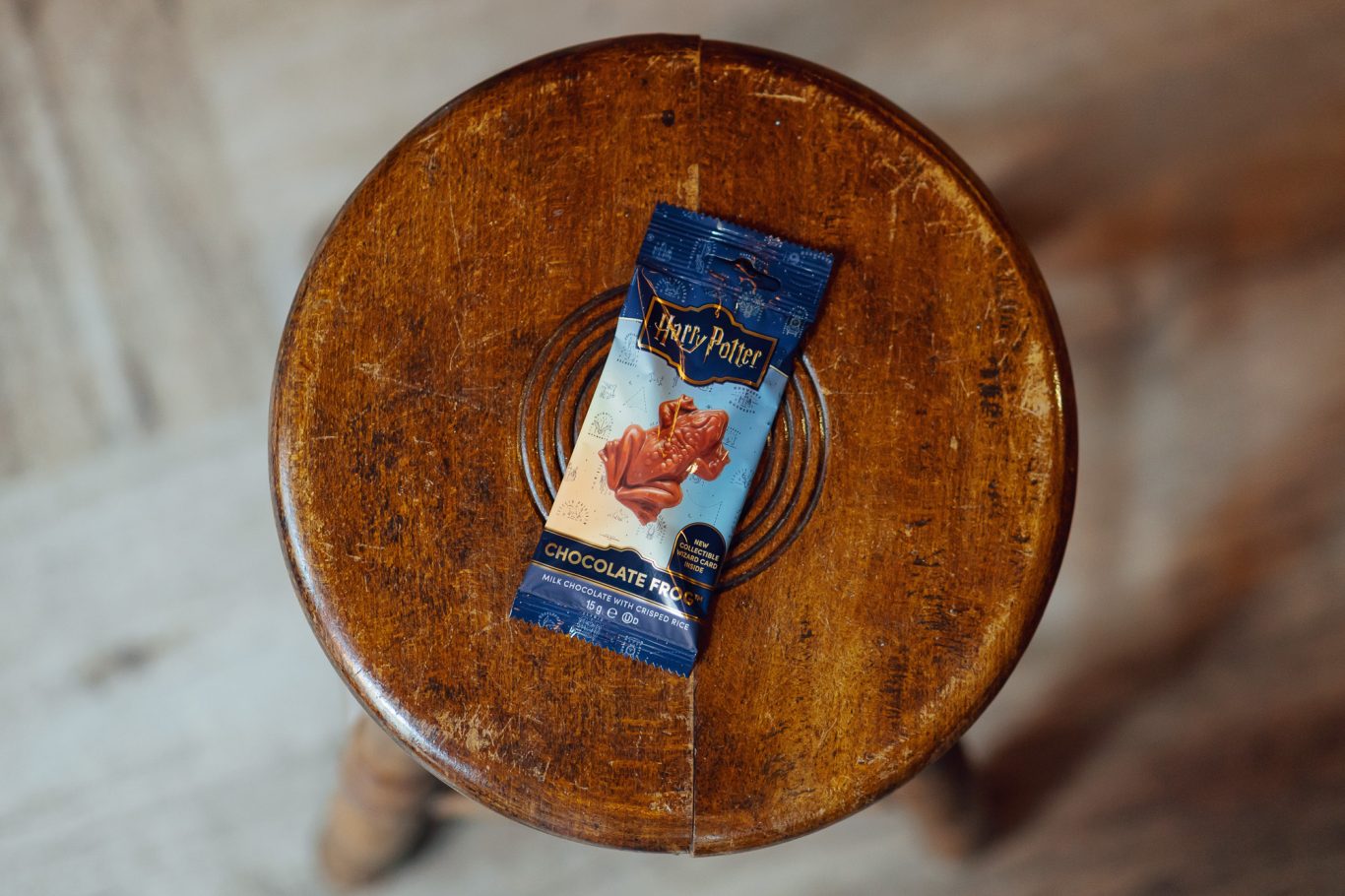 Schokofrosch mit Hologramkarte Ein verpackter Schokofrosch liegt auf einem Hocker.